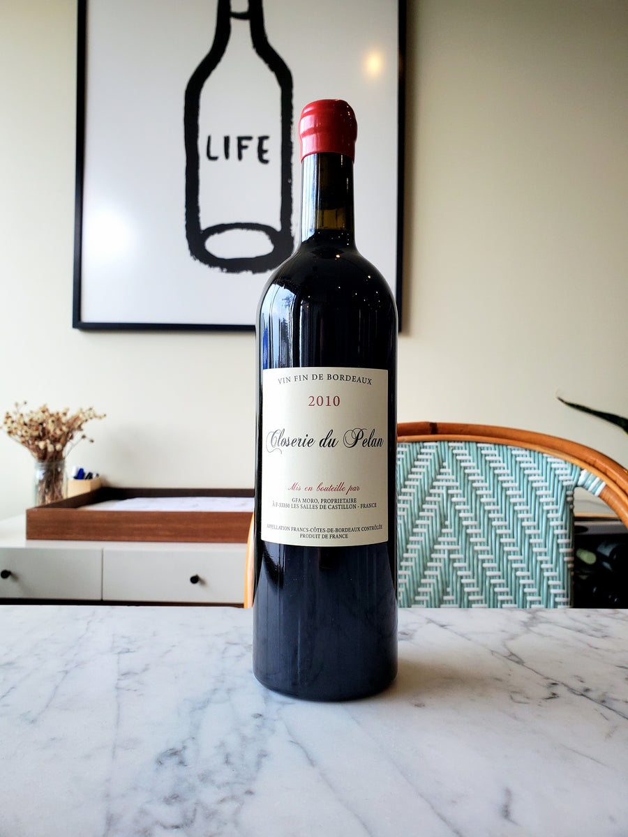 A bottle of Closerie du Pelan Bordeaux Rouge, France 2010, placed on a marble countertop with a decorative item and a framed picture in the background.