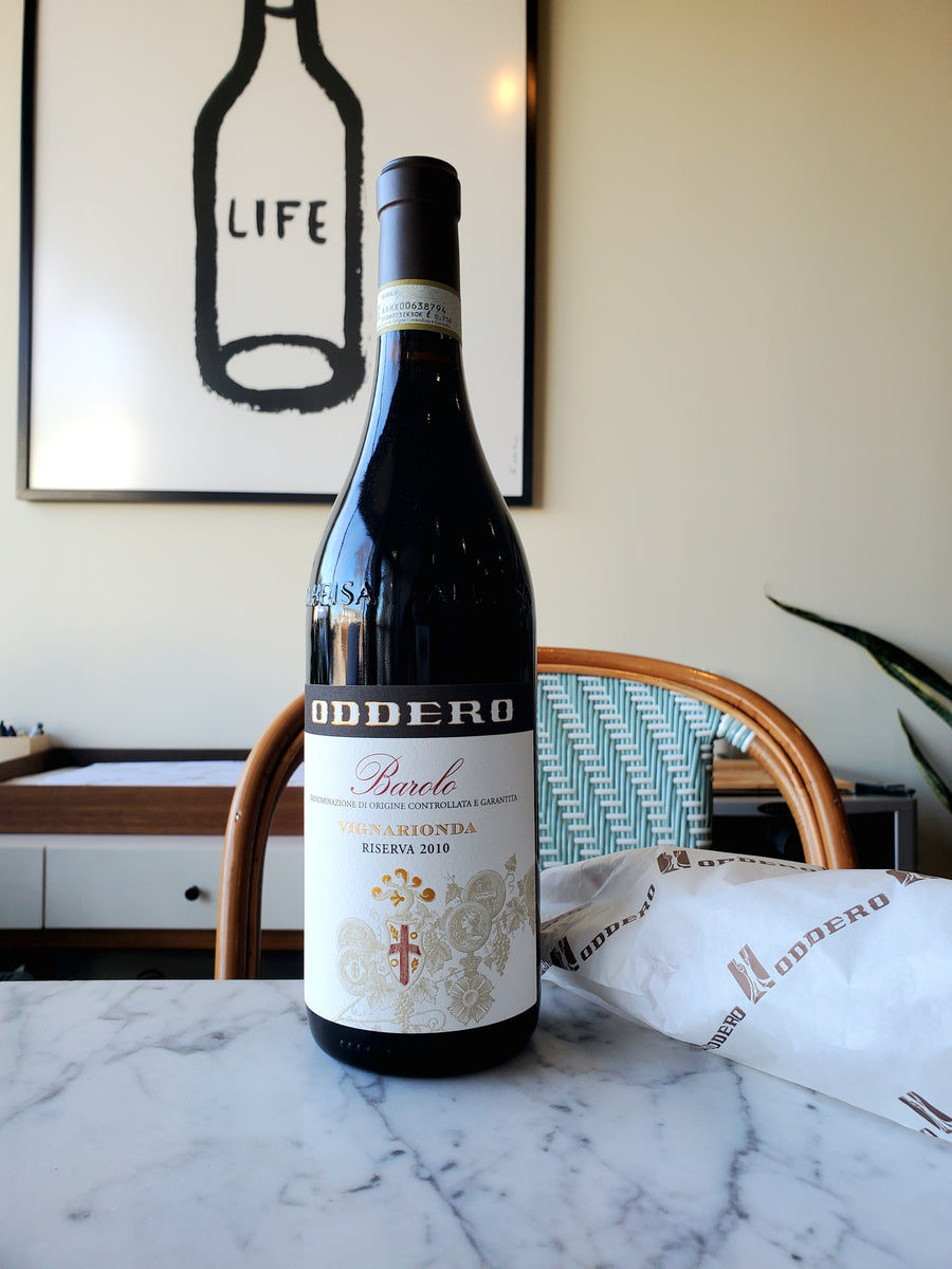 A bottle of Oddero Vignarionda Barolo, Italy 2010 red wine placed on a marble surface with a framed artwork 'LIFE' on the wall in the background.